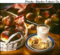 A basket full of sweet buns, a plate with a bun and a glass of milk next to it and a tray with more buns in the background.