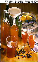 Four glass bottles and three glasses filled with mead; raisins on the table and lemons in the background.
