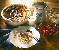 A table set with a bowl of oven porridge topped with milk, a jug of milk and a bowl of berries. 
