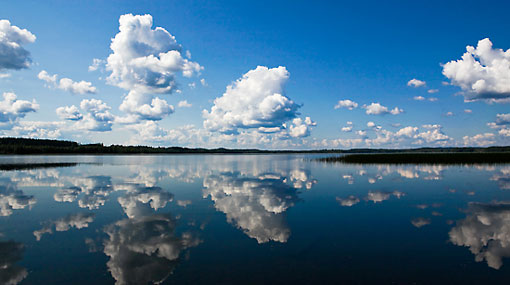 A clear lake reflecting the cumulus clouds above.