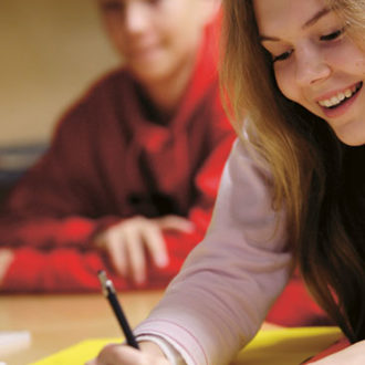 A smiling student writing on a paper.