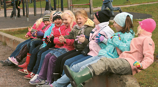 A group of laughing pupils sitting on a fence outside.