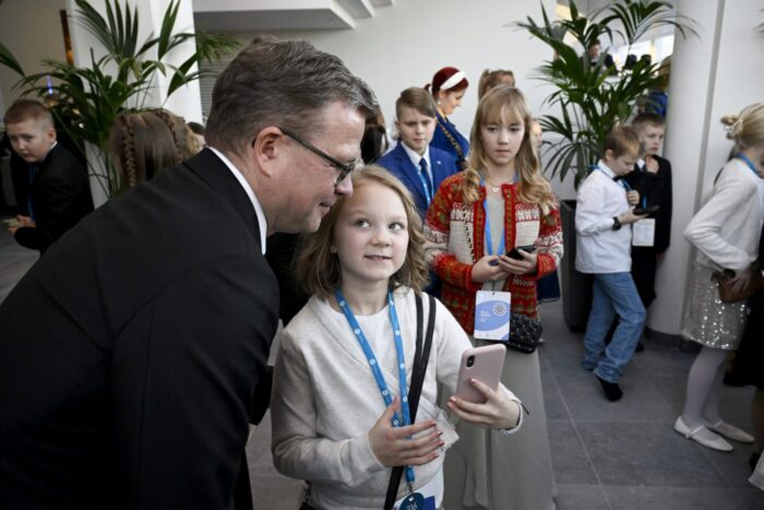 A man in a suit bends down so that a schoolchild can take a selfie with a mobile phone.