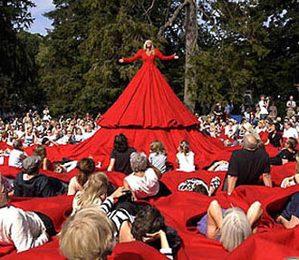 A character in a red dress; people sitting on the huge hem of the dress.