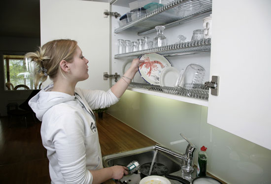 A woman placing dishes to a dish-drying cupboard.