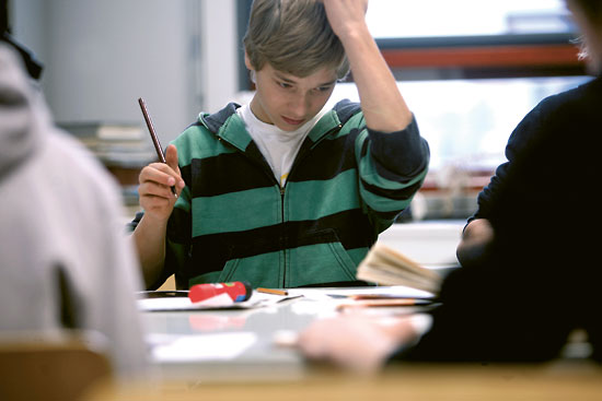 A thoughtful-looking student with pencil in hand looking at papers in front of him.