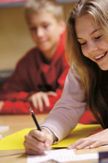 A smiling student writing on a paper.