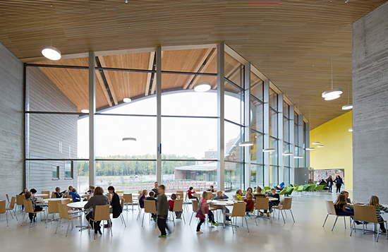 Schoolchildren sitting at tables in a light open space with floor to ceiling windows.