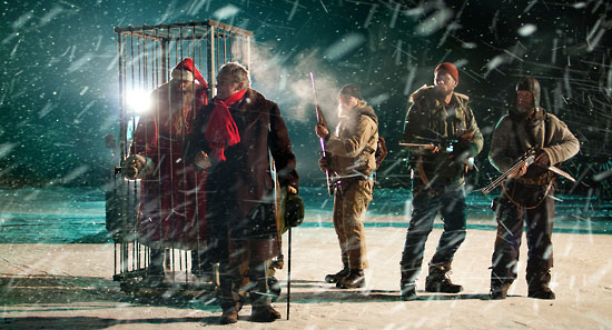 Three armed men guarding Santa Claus trapped in a cage.