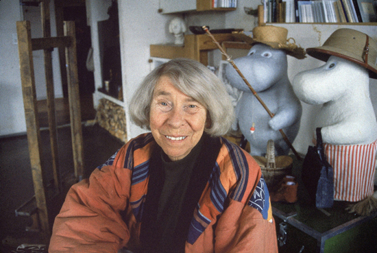 Photo of elderly Tove Jansson sitting next to two Moomin plushies.