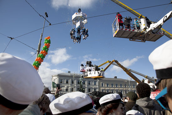 A group of university students being lift up by a crane; a group of other students watching.