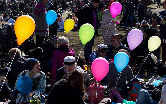 A large crowd of people picknicking at a park with colourful balloons.