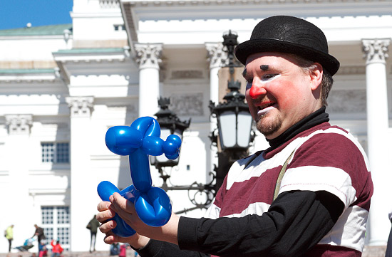 A smiling clown creating balloon figures in front of Helsinki Cathedral.