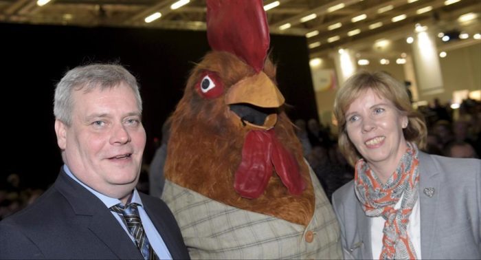 社会民主党主席安蒂·林内（左）和司法部长安娜-玛雅·亨里克森（Anna-Maja Henriksson，右，瑞典族人民党）在最近举办的教育展会上与一只“大公鸡”（中，所属政治党派不明）合影。