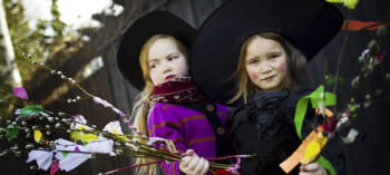 Two children dressed as witches with a bunch of decorated willow twigs in hand.