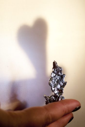 A person holding a piece of melted tin; the tin making a heart-shaped shadow on the wall.