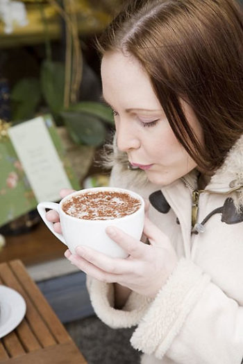 A woman holding a large cup of cappuccino with two hands.