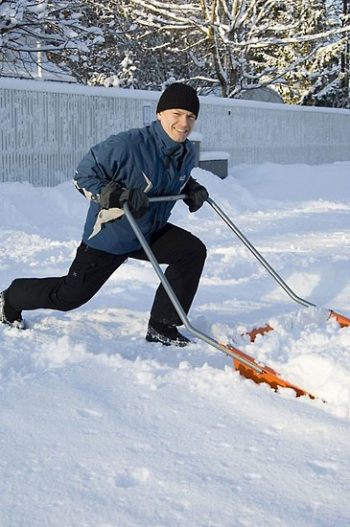A smiling man pushing a snow scoop filled with snow.