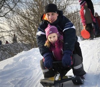 A man and a child are sitting on a sled, sliding down a snowy hill.