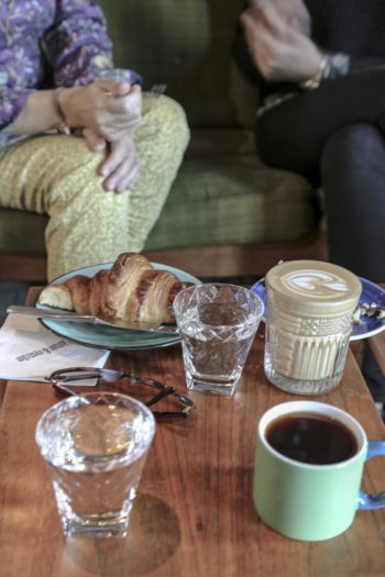 A coffee table set with cups of coffee, glasses of water and a croissant.