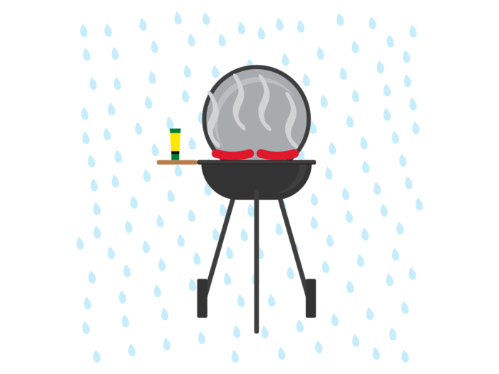 A black kettle barbecue grill is standing in the rain with two steaming sausages cooking on it.