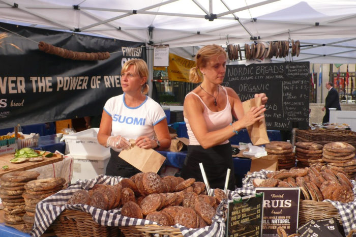 Two vendors at a market stall with piles of rye bread on sale. 