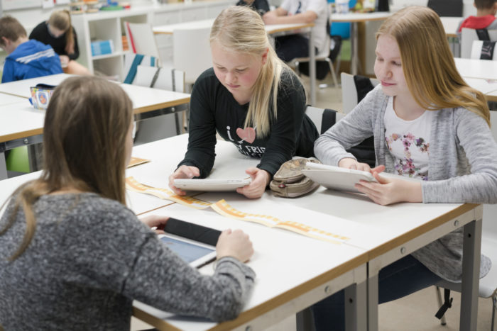 Three girls studying tablets in a classroom.