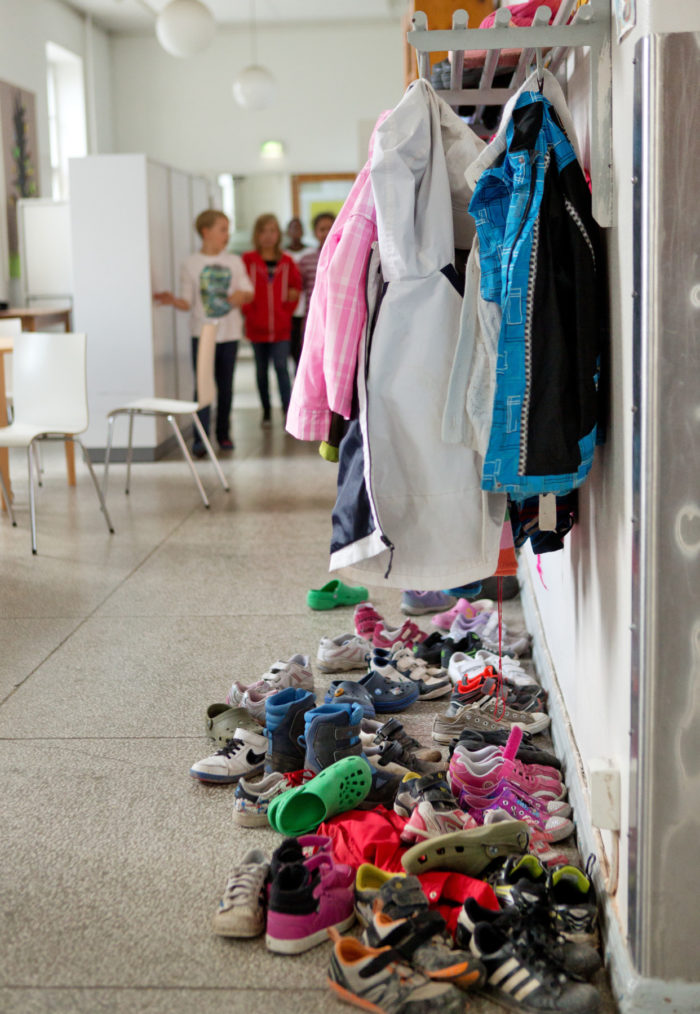 Jackets hanging from a rack; a pile of children's shoes on the floor.