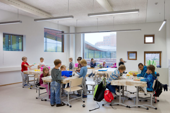 Schoolkids studying and dabbling in a light classroom with big windows.