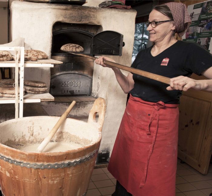 A woman taking a rye bread out of a big baking oven.