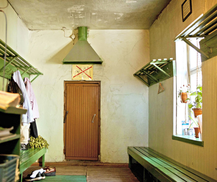 Раздевалка в старинном здании с зелеными скамейками и банными вениками вдоль стен.