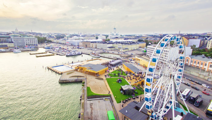 An aerial photo of Helsinki market square and harbor shows a pier with swimming pools and a white and blue Ferris wheel.