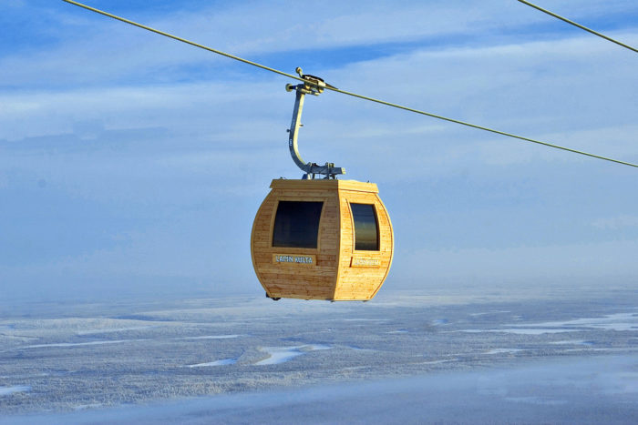 A gondola ski lift is hanging from a cable above a snowy landscape.