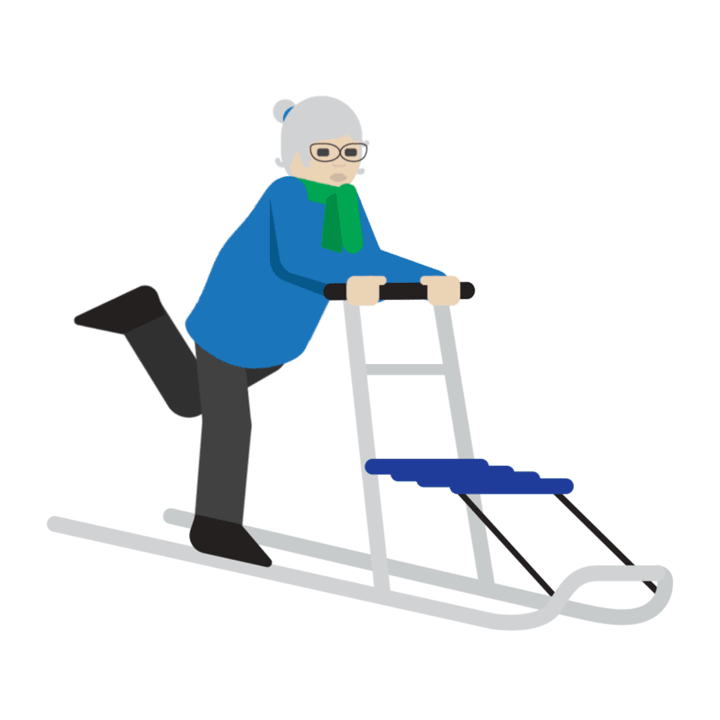 An elderly woman stands on a kicksled, pushing off with one foot and pointing forward with her left index finger.