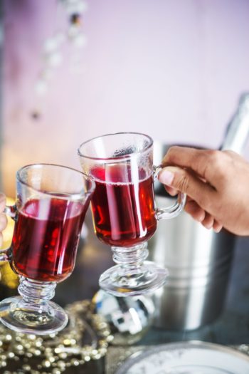一只手握着一个玻璃杯，正与另一只杯子碰杯，两只杯子里都盛满相同的红色液体。