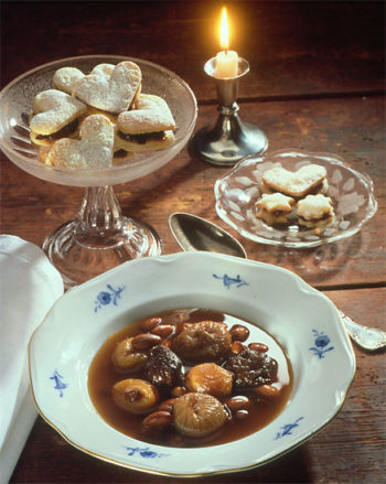 A bowl containing fruit soup is flanked by platters of cookies.