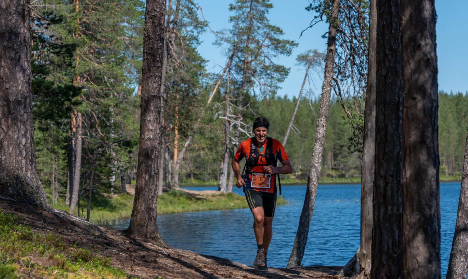 A man runs along a forested trail by a lake.