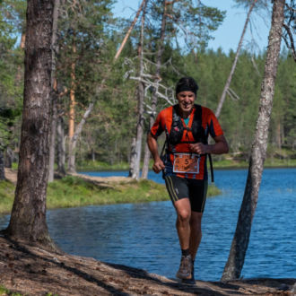 A man runs along a forested trail by a lake.