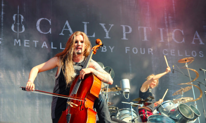 A long-haired man playing the cello on a stage, a drummer in the background.