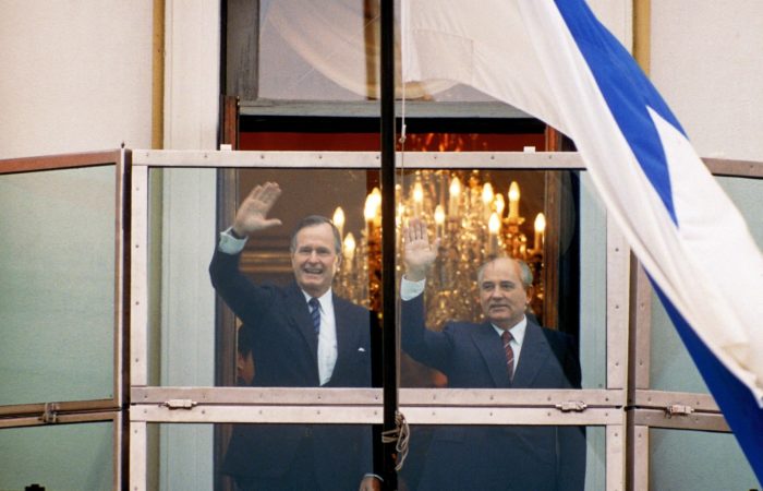 Smiling George H.W. Bush and Mikhail Gorbachev waving from a balcony.