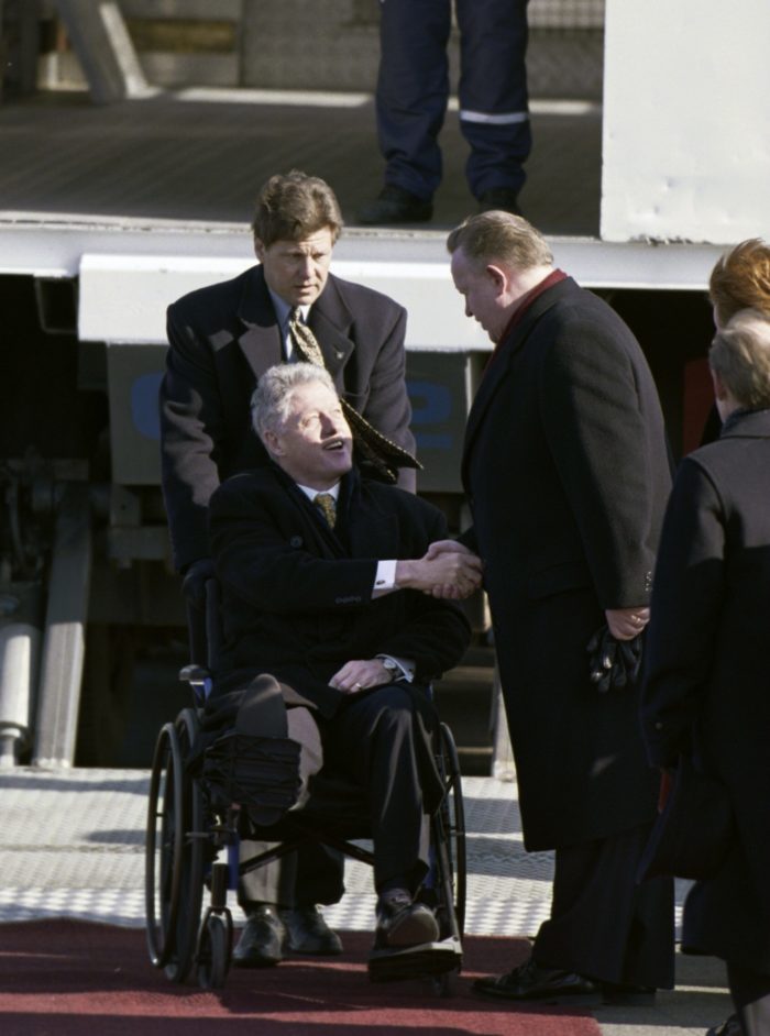 Martti Ahtisaari shaking hands with Bill Clinton sitting in a wheelchair.