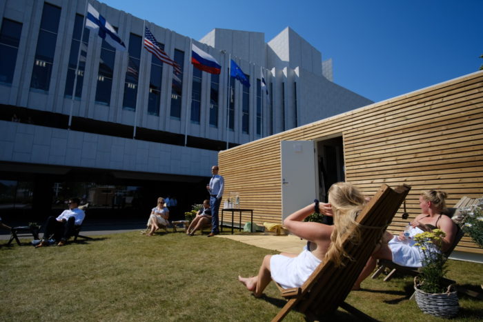 People sitting in the sun outside of a wooden container sauna.