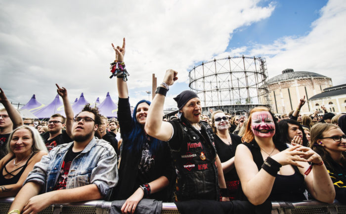 Several metal fans dressed in genre gear wave their hands at a concert.