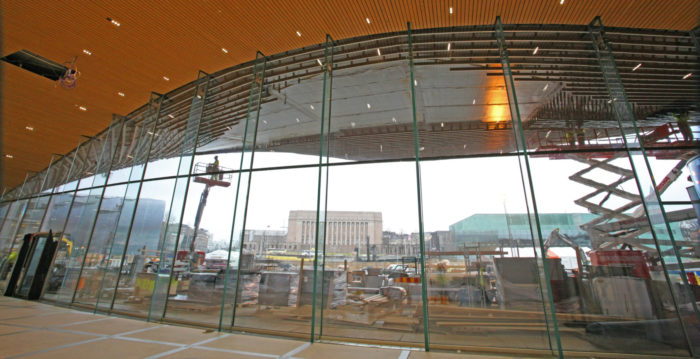 على أحد جانبي مكتبة Oodi، يظهر على المحيط المنحني من إطارات النوافذ المباني القريبة من متحف كايزما للفن المعاصر (على اليسار)، والبرلمان (في الوسط)، والمركز الموسيقي (على اليمين).