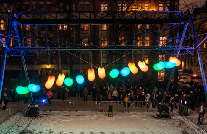 Colourful round lights hanging in a railing, a crowd gathered to watch them.