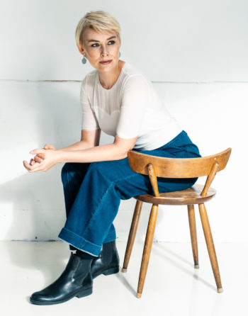 Portrait of author Laura Lindstedt sitting on a chair wearing blue jeans and a white t-shirt.