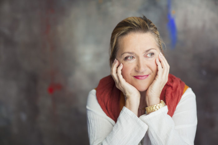 Portrait of author Anja Snellman leaning her face in her hands and looking to right.