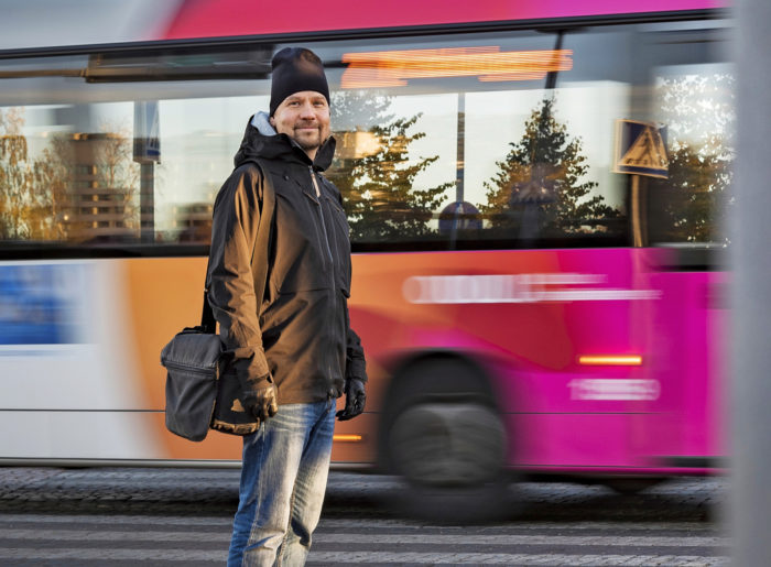 Portrait of a man standing by a crosswalk, with a moving bus in the background.