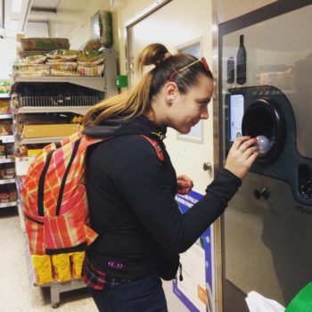 A woman putting bottles in a recycling machine at a grocery store.