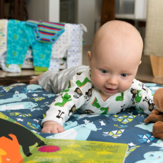 A small baby lying on the floor on a blanket looking at a children's book.